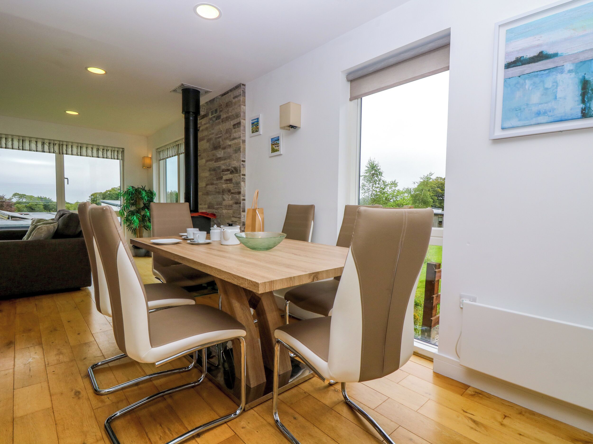 A modern dining area with a wooden table, cushioned chairs, and a view of the outdoors through large windows.