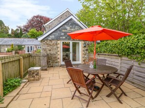 A stone house with a patio featuring a table and chairs, an umbrella, and a wooden fence. - Cornflower Cottage (St. Columb Major)