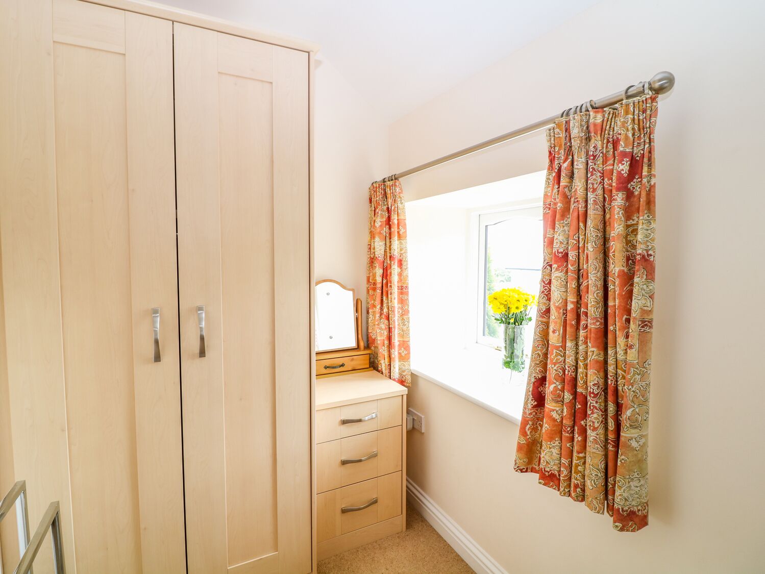 Une chambre à coucher comprenant une armoire, une coiffeuse avec un miroir, une commode et une fenêtre avec des rideaux.