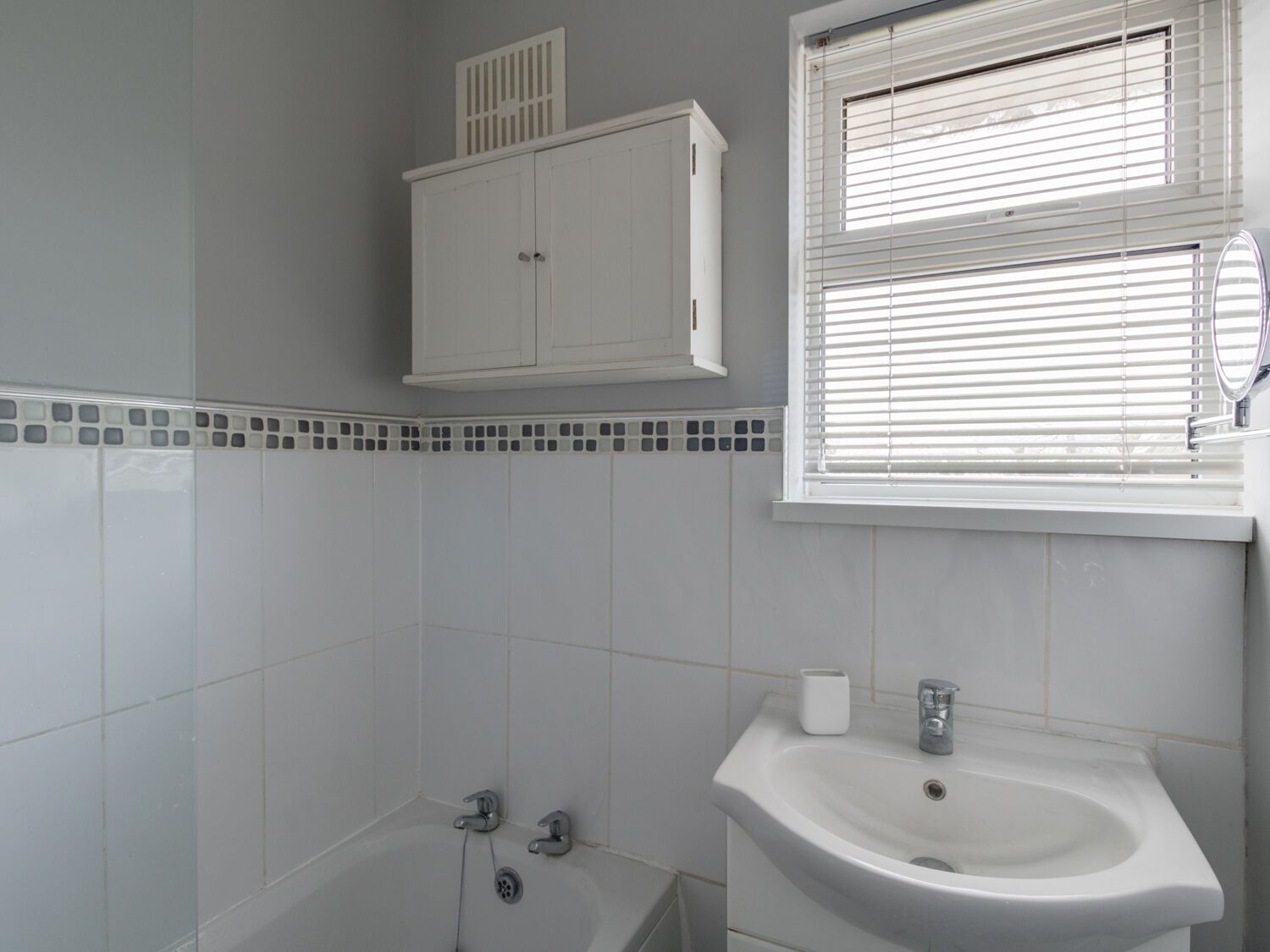 A bathroom with a bathtub, a sink, and a window with blinds.