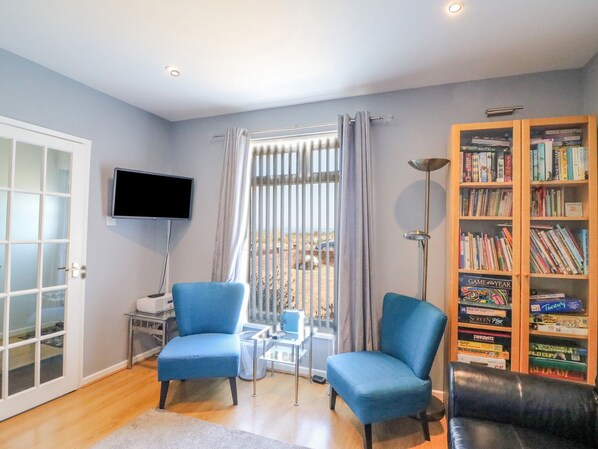 A living room with two blue armchairs, a bookshelf, a television, and a window with curtains.