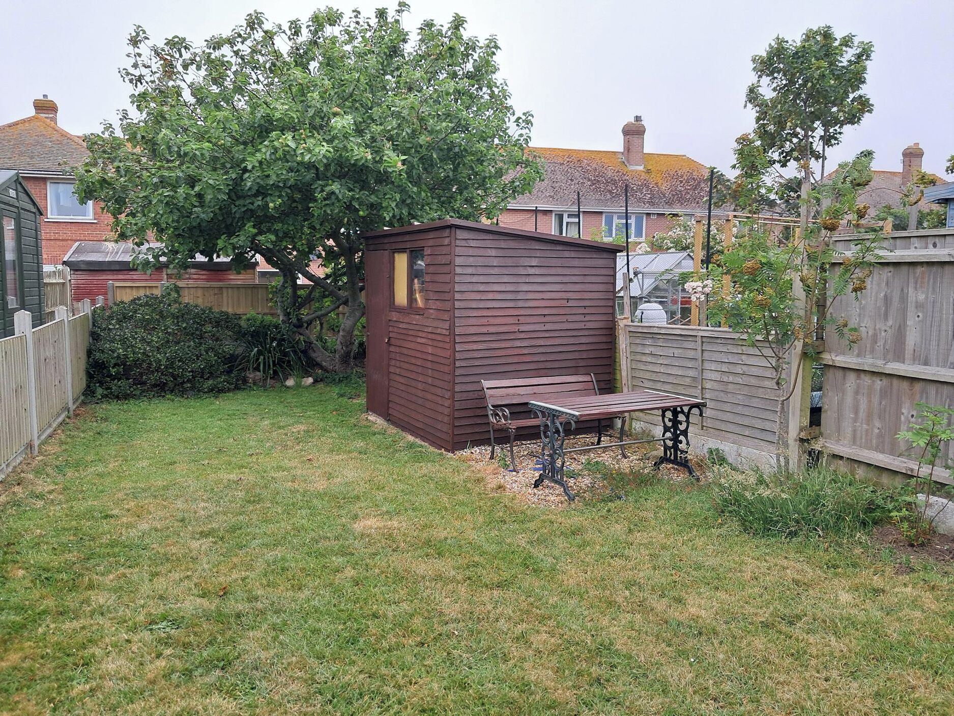 A small wooden shed with a bench in a backyard.