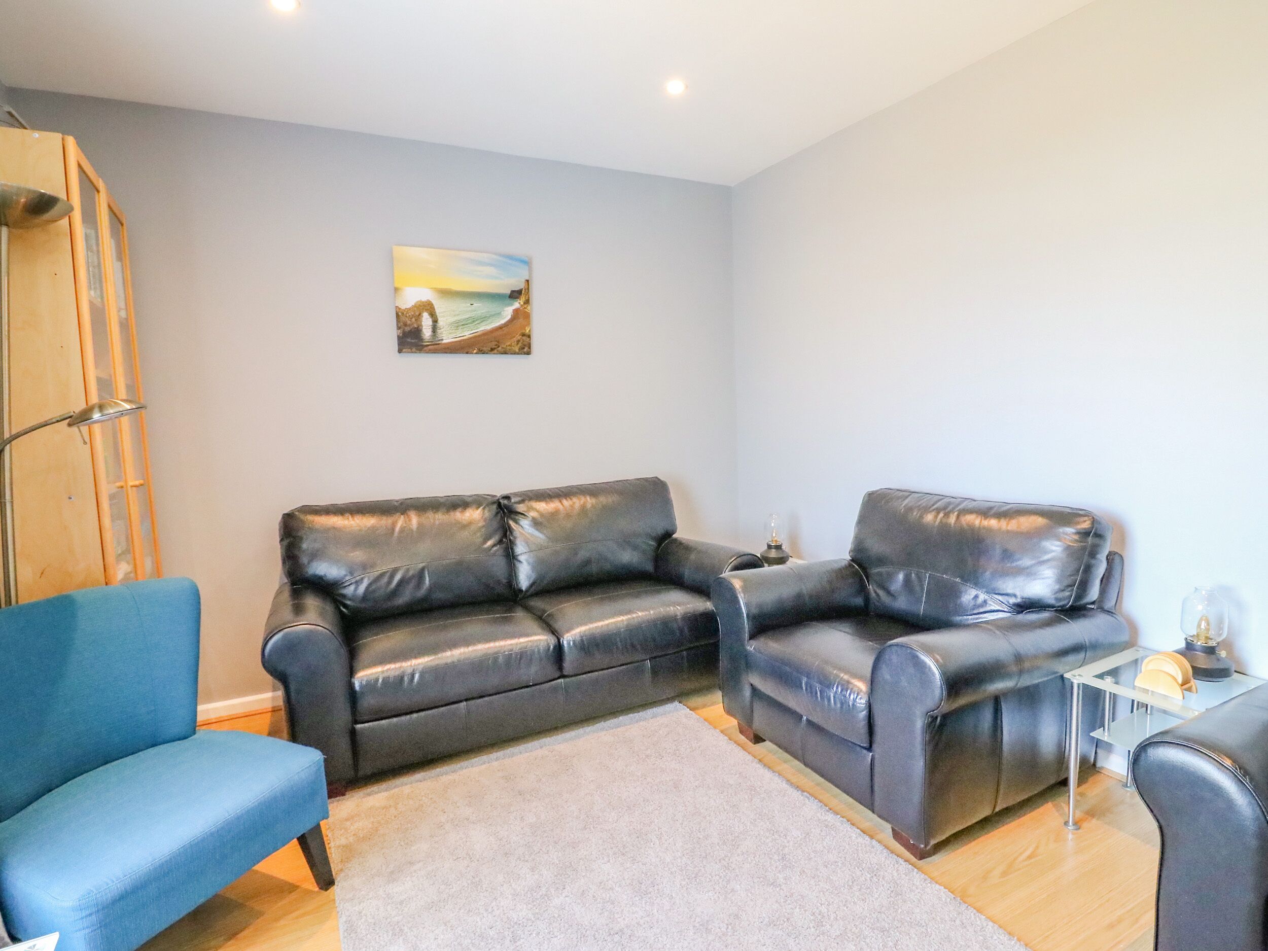 A modern living room with a blue armchair, a black leather sofa, and a small side table with a lamp.
