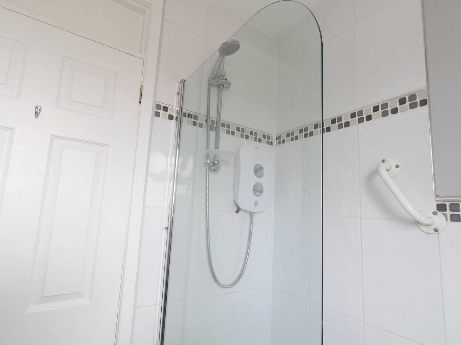 A glass-enclosed shower with a handheld showerhead and a wall-mounted control panel.