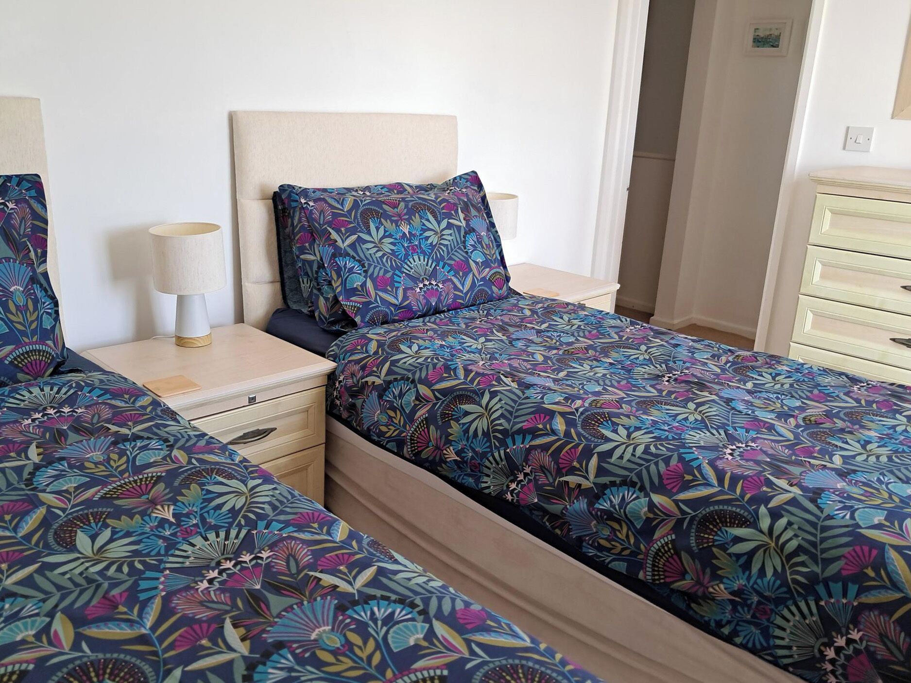 A bedroom with two beds, a nightstand, a dresser, and a lamp.