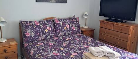 Un dormitorio con cama, televisor, mesita de noche, lámpara y cómoda.