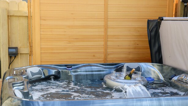 Ein Whirlpool mit einer hölzernen Sitzbank davor, umgeben von Holzwänden.