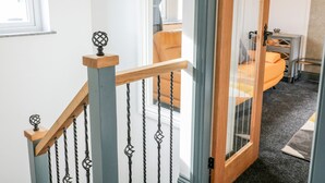 Eine Treppe mit hölzernem Geländer und Metallspindeln, die zu einem Zimmer mit einem Bett und einem kleinen Tisch führt.