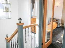 Uma escadaria com corrimão de madeira e balaústres de metal, que leva a um quarto com uma cama e uma mesinha.