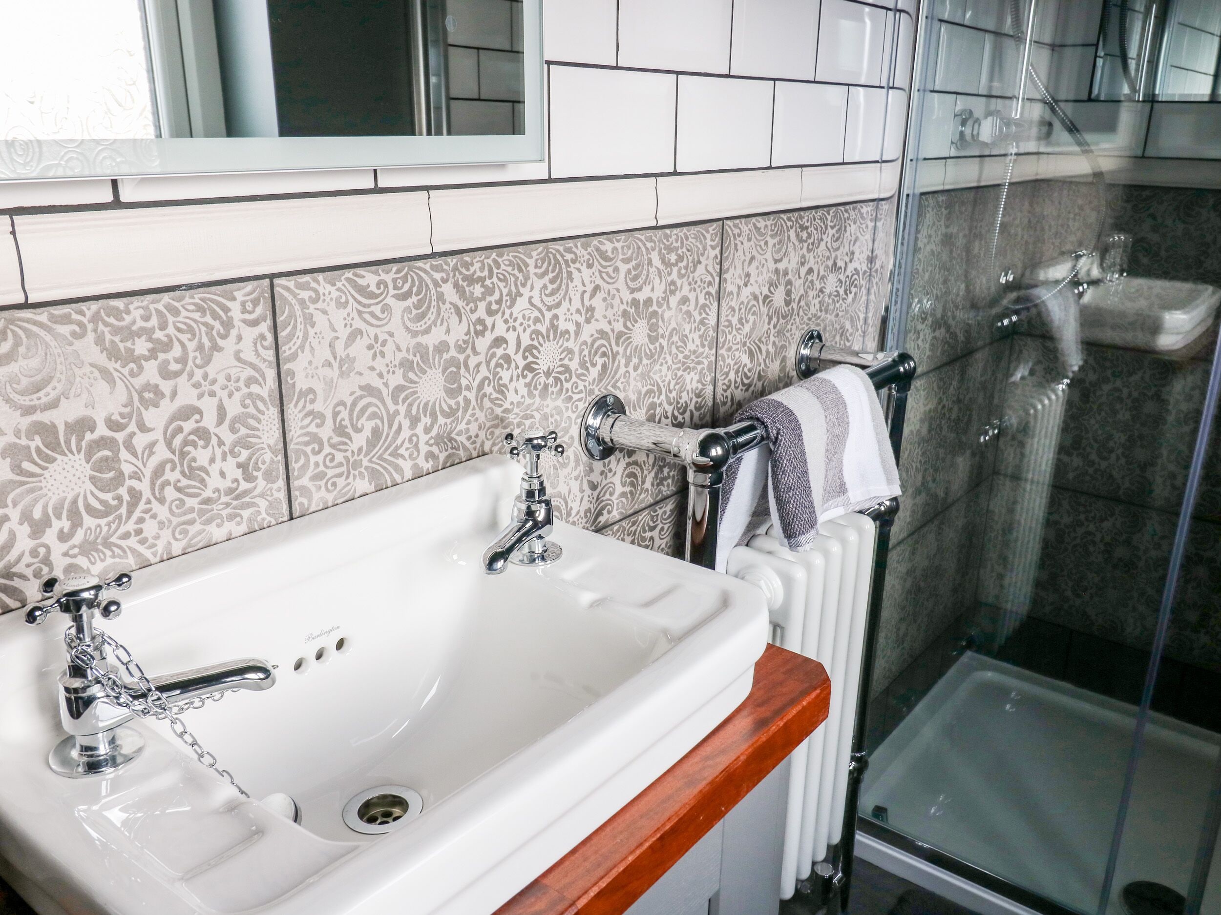Une salle de bain avec un lavabo blanc, un plan de travail en bois, une douche avec une porte en verre et des carreaux décoratifs sur les murs.