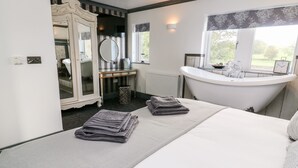 Ein Schlafzimmer mit einem großen Bett, einem Schminktisch mit Spiegel, einer Badewanne und Blick ins Freie.