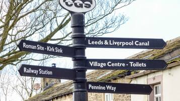 A directional signpost with multiple arrows pointing towards various destinations such as Roman Site, Kirk Sink, Leeds & Liverpool Canal, Village Centre, Railway Station, and Pennine Way.