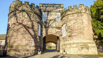 A historic stone castle entrance with a sign reading "DE'S OF MATS".