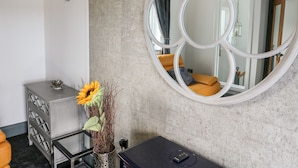 Ein modernes Badezimmer mit einem großen Spiegel, einer Vase mit Sonnenblumen, einem grauen Schrank und einem schwarzen Massagetisch.