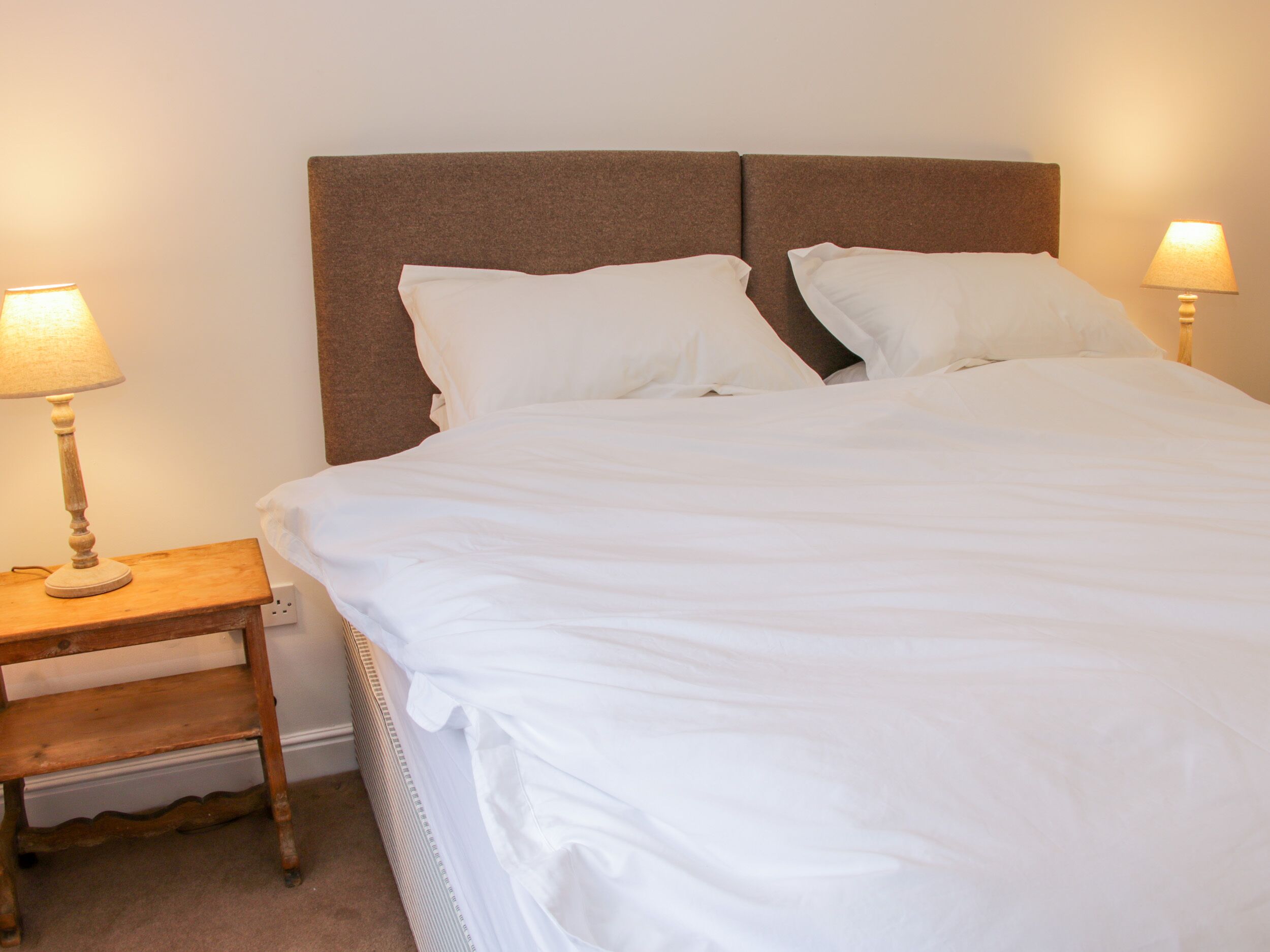 A neatly made bed with white linens, two bedside lamps, and a wooden nightstand.