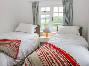 A bedroom with two beds, a window with curtains, and a bedside table with a lamp.