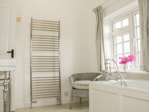 A bathroom with a white sink, a bathtub, a towel rack, a wicker chair, and a window with curtains.