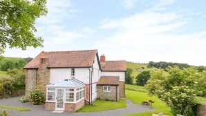 A traditional stone house with a conservatory, surrounded by a well-maintained garden and a rural landscape.