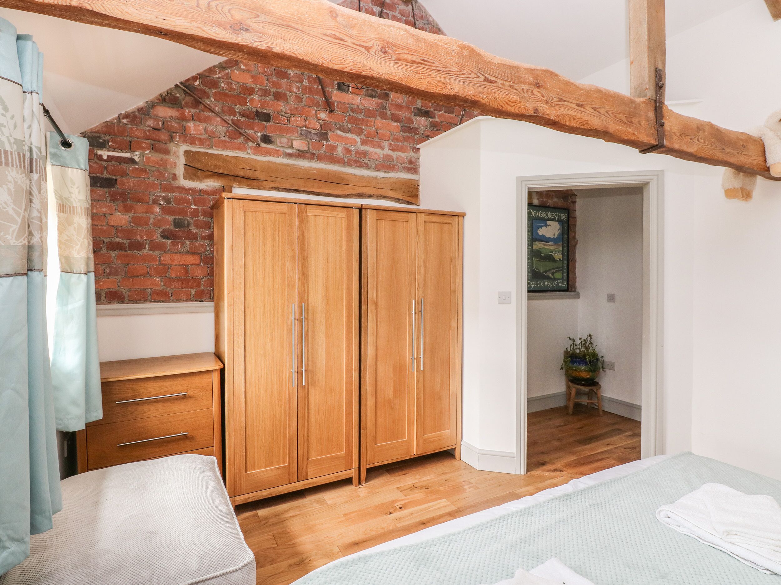 A bedroom with wooden wardrobe, a bed, and a brick wall.