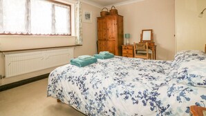 Quarto com uma cama grande, guarda-roupa de madeira, escrivaninha com cadeira e radiador.