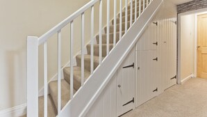 A staircase with beige carpeted steps and white railings, leading to a room with a wooden door and a stone accent wall. - Harley House (Broughton in Furness)