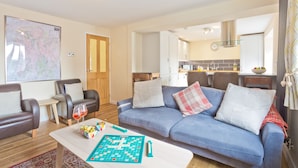 A living room with a sofa, coffee table, and a board game. There is a map on the wall and a door leading to the kitchen. - Harley House (Broughton in Furness)