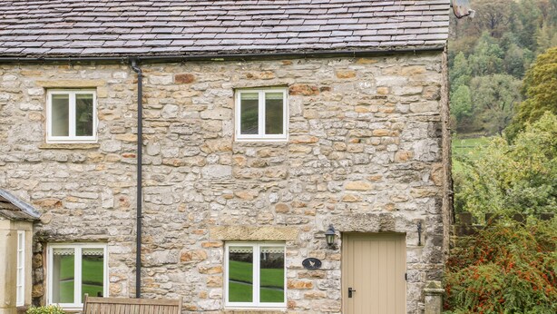A stone building with two windows, a door, and a bench outside. - Croft Cottage (Skipton)