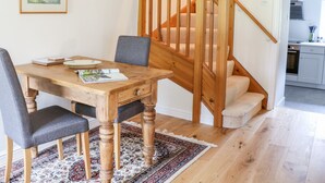 A dining area with a wooden table and chairs, a rug, and a staircase leading to an upper level. - Croft Cottage (Skipton)