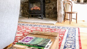 A cozy room with a stone fireplace, a wooden chair, and a small table with books. - Croft Cottage (Skipton)