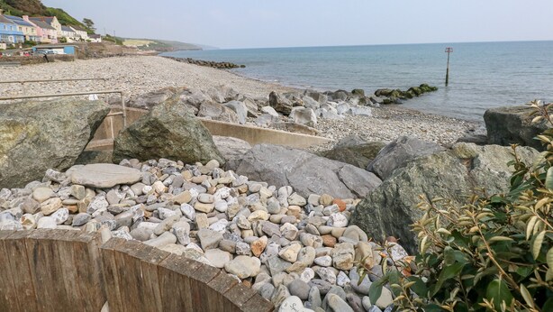 A rocky beach with a wooden fence and a red buoy in the water. - Potters Barn (Kilgetty)