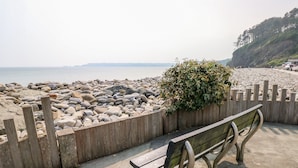 A bench by a rocky beach with a wooden fence and a small bush. - Potters Barn (Kilgetty)