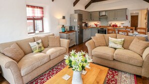 A spacious living area with two sofas, a wooden coffee table, and a kitchen in the background. - Potters Barn (Kilgetty)