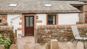 A traditional stone house with a sloped roof, a wooden door, and a small window. - The Old Cook House (Penrith)