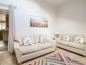 Ein Wohnzimmer mit zwei beigen Sofas, einem gemusterten Teppich und einem Blumenbild an der Wand.