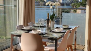Une table à manger dressée pour quatre personnes, avec des chaises blanches, un vase rempli de fleurs blanches et une bouteille de champagne.