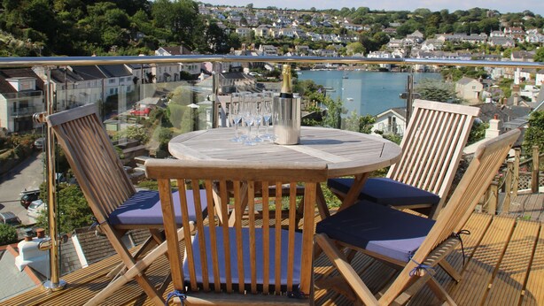 Une terrasse en bois avec une table ronde et des chaises, donnant sur un quartier résidentiel et un plan d’eau.