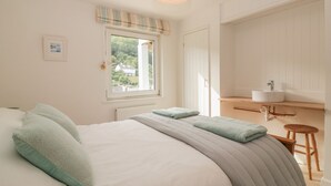 Une chambre avec un grand lit, une fenêtre donnant sur un beau paysage, une table de chevet et un petit tabouret.