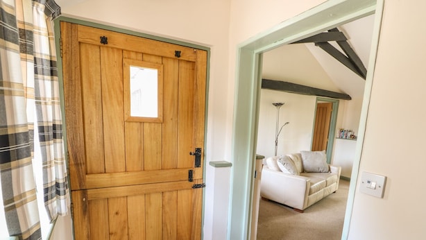 A wooden door with a small window, a checkered curtain, and a tiled floor leading to a living room with a white sofa and a lamp. - The Bull Pen (Eye)