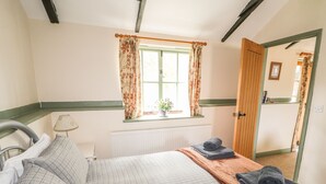 A bedroom with a bed, a window with floral curtains, a radiator, and a wooden door. - The Bull Pen (Eye)
