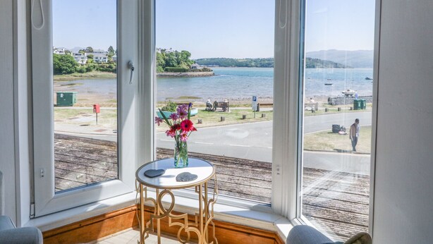A room with a large bay window overlooking a waterfront. - Bay View Apartment (Porthmadog)