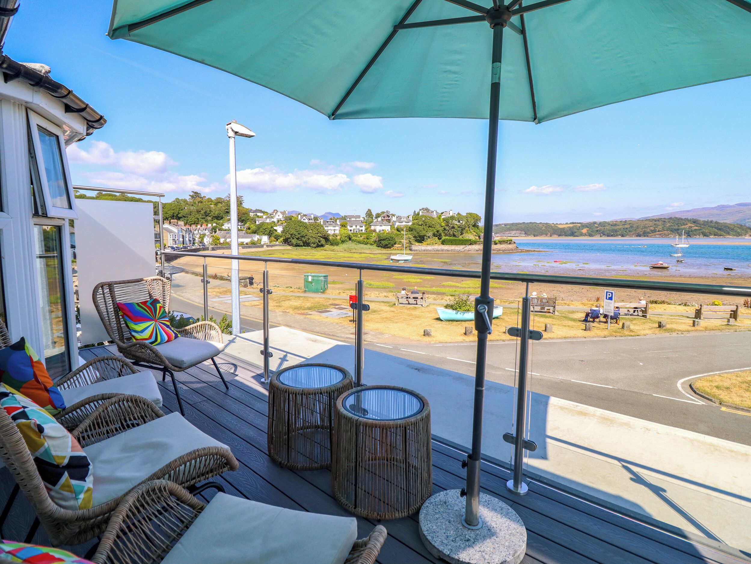 A deck with wicker furniture and a view of a beach and ocean.