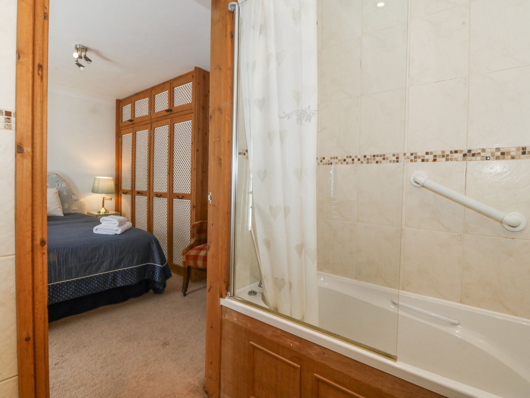A bedroom with a bed, a nightstand, a wooden partition, and a shower area with a grab bar.