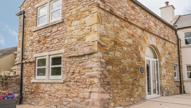 A stone building with a traditional architectural style, featuring a large arched doorway and a small window. - The Barn (Workington)