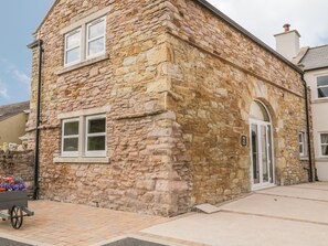 A stone building with a traditional architectural style, featuring a large arched doorway and a small window. - The Barn (Workington)