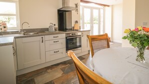 A kitchen with a built-in oven, a sink, and a window. There is a dining table with chairs and a vase of flowers. - The Barn (Workington)