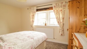 A bedroom with a bed, a wooden wardrobe, a window with curtains, and a radiator. - The Barn (Workington)