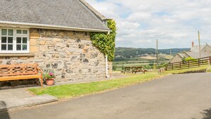 A stone house with a sloped roof, a wooden bench, and a potted plant in front. - Coquet View Cottage (Morpeth)