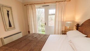 A bedroom with a bed, a nightstand, a lamp, a window with curtains, and a framed picture on the wall. - Coquet View Cottage (Morpeth)