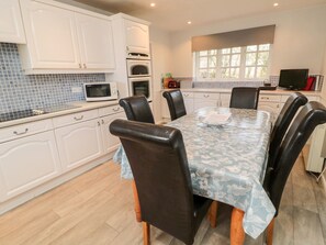 A modern kitchen with white cabinets, a dining table with floral tablecloth, and a large window.