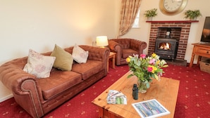 A living room with a brown leather sofa, a wooden coffee table with magazines, and a fireplace. - Coquet View Cottage (Morpeth)